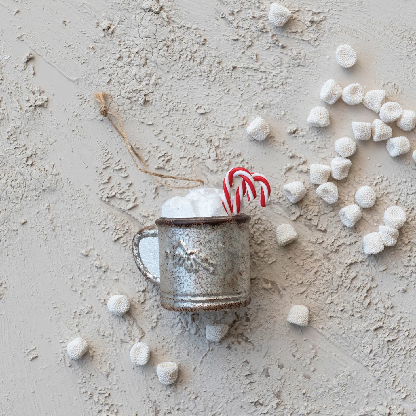 glass Mug Ornament with Candy Canes laying on a plaster surface with marshmallows scattered about.