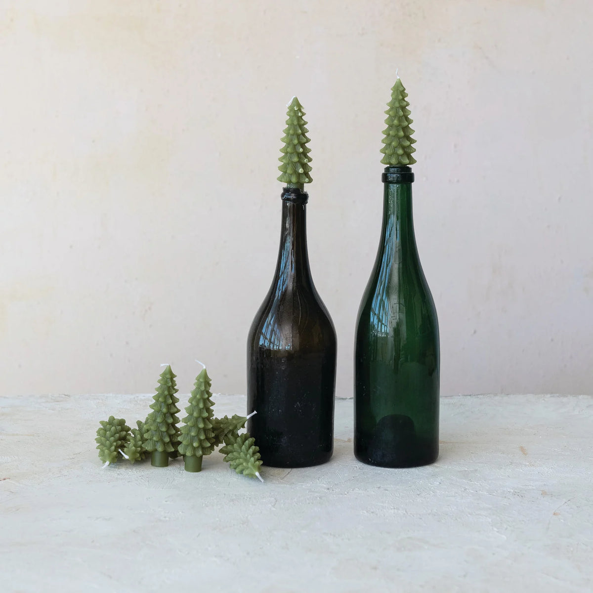 tree shaped candles in a pile next to 2 tree candles in glass bottles