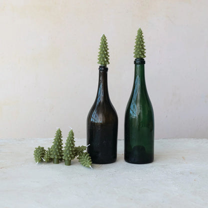 tree shaped candles in a pile next to 2 tree candles in glass bottles