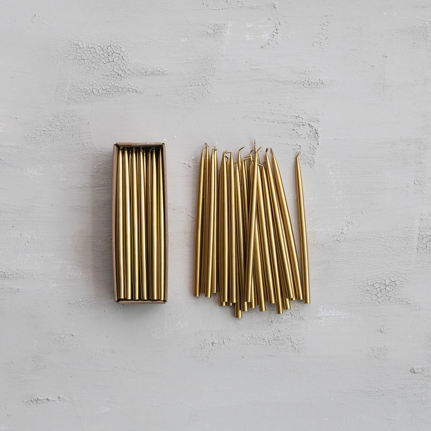 Thin Gold Taper Candles arranged both in and out of their box packaging