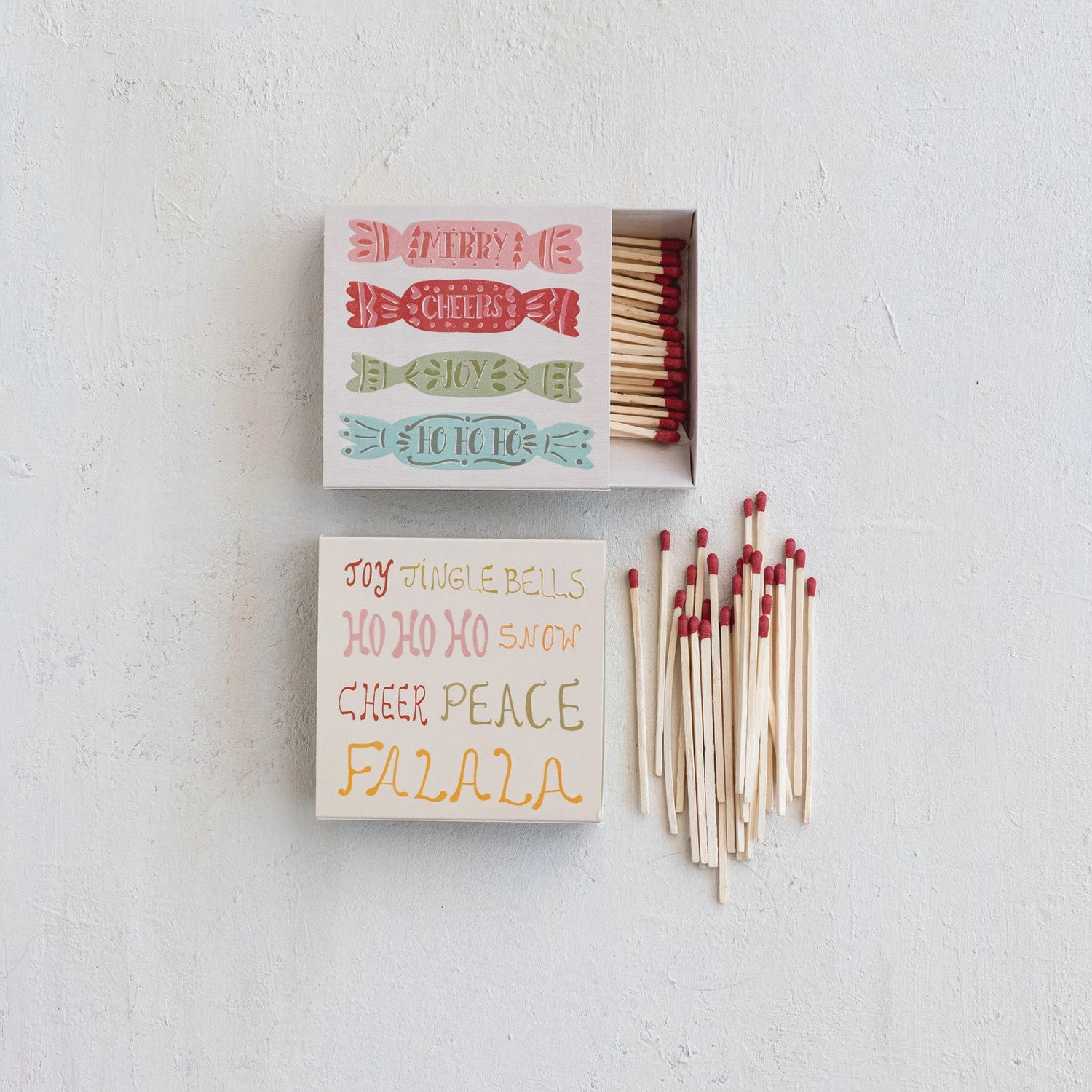 2 styles of Holiday Matches on a table with matches one has candy design, the Christmas words
