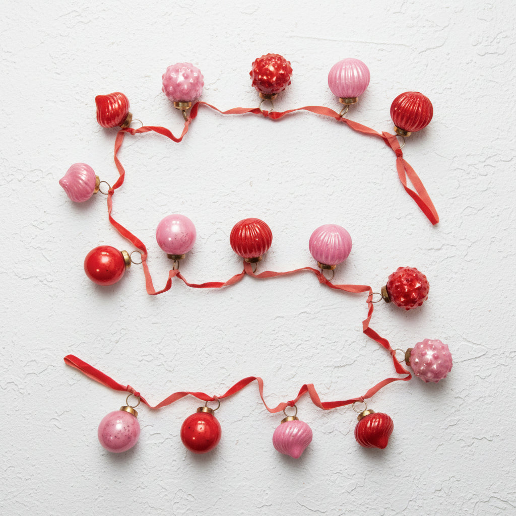 red velvet ribbon with pink and red mercury ornaments attached to it and draped on a plaster surface