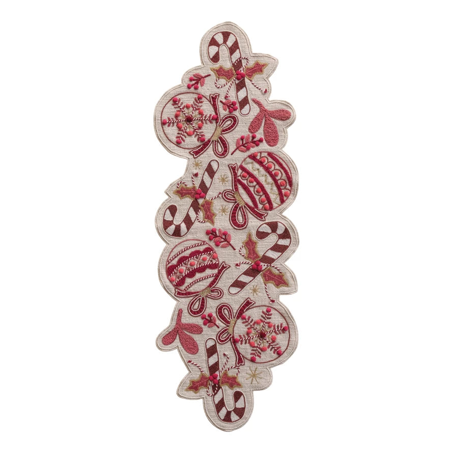 red stitched and beaded ornament, foliage, and candy canes on a taupe runner