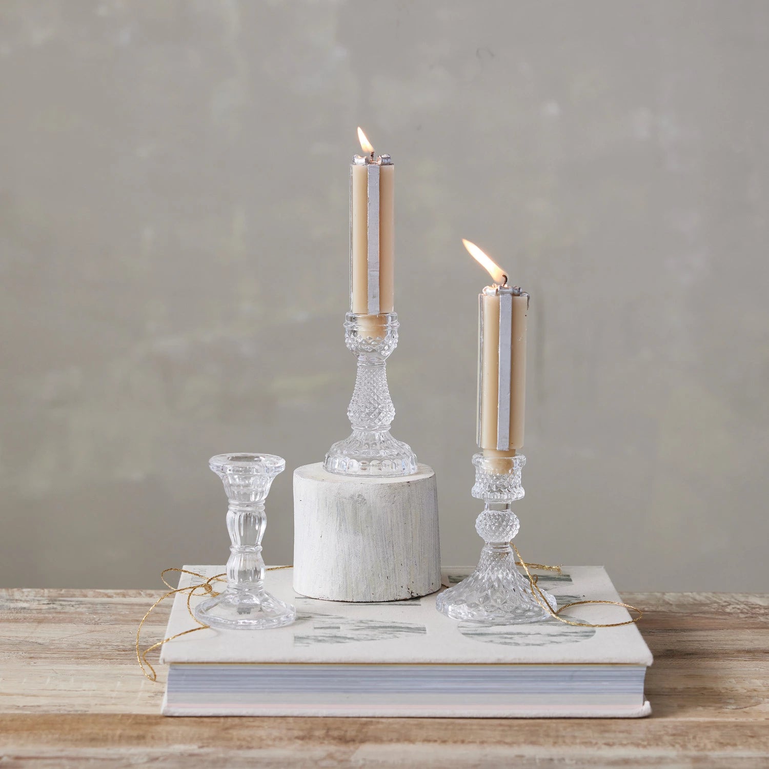 3 Pressed Glass Taper Holders  with lit tapers in them arranged on a table with books and gold ribbon