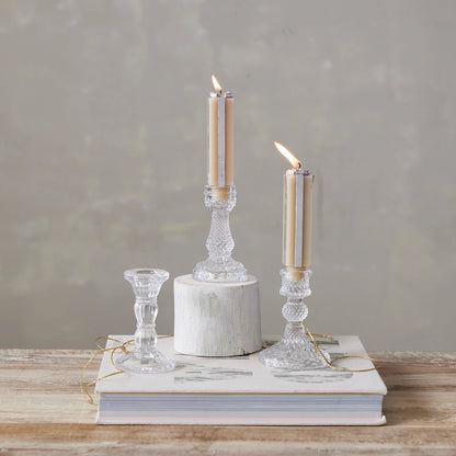 3 Pressed Glass Taper Holders  with lit tapers in them arranged on a table with books and gold ribbon