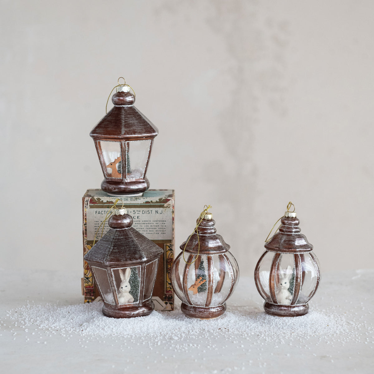 4 lantern ornaments arranged on a grey background with a sprinkling of artificial snow