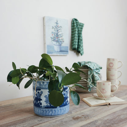 blue and white planter with a plant in it on a decorated table with a stack of dishes in the background