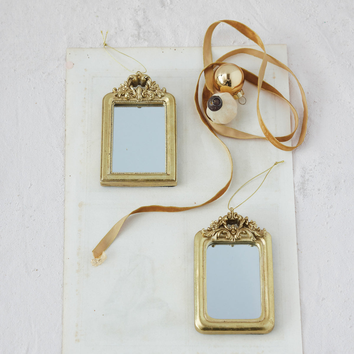 2 gold framed mirror ornaments on a decorated surface