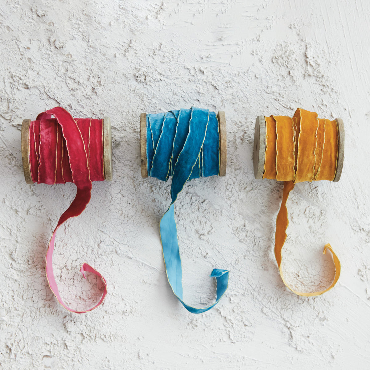 red, blue, and yellow ribbon on wooden spools on a plaster background