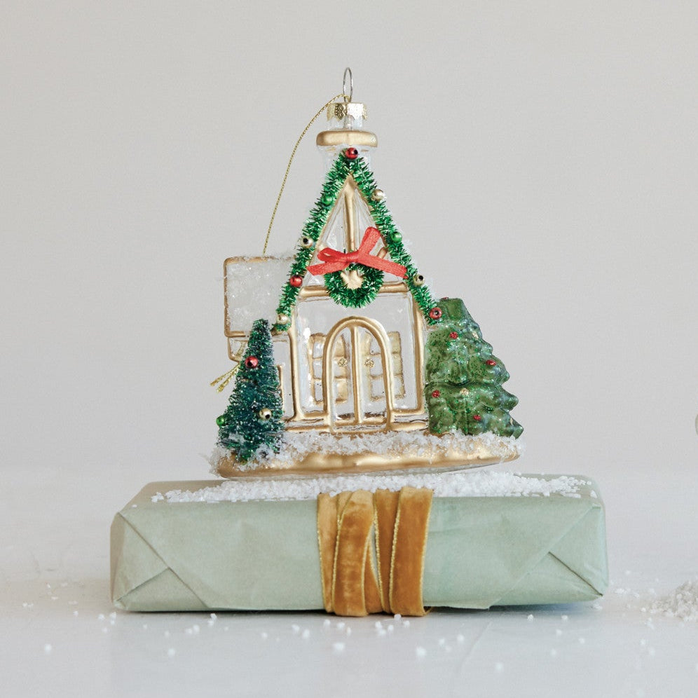 glass church Christmas ornament set on a wrapped gift with artificial snow sprinkled about 