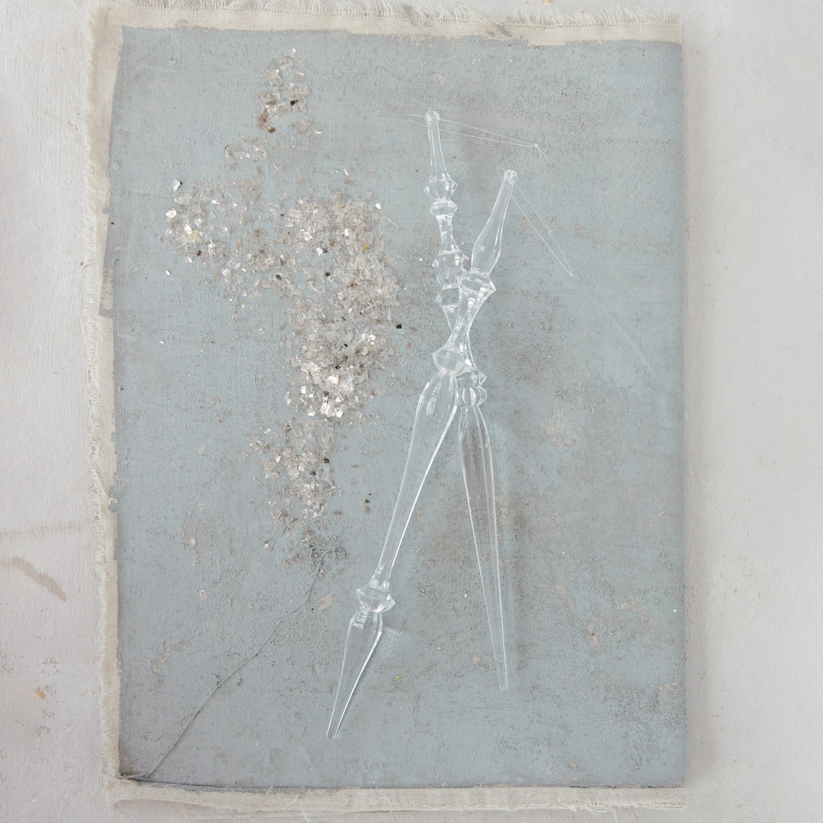 2 acrylic icicles laying on a stack of grey paper with a sprinkling of silver glitter next to them