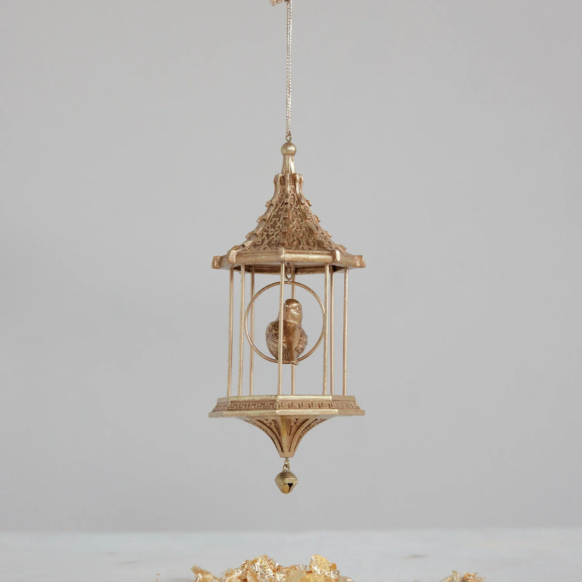 gold birdcage ornament with little gold bird inside hung front of a light grey wall