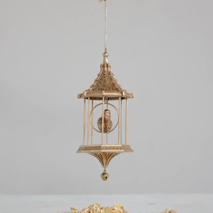 gold birdcage ornament with little gold bird inside hung front of a light grey wall