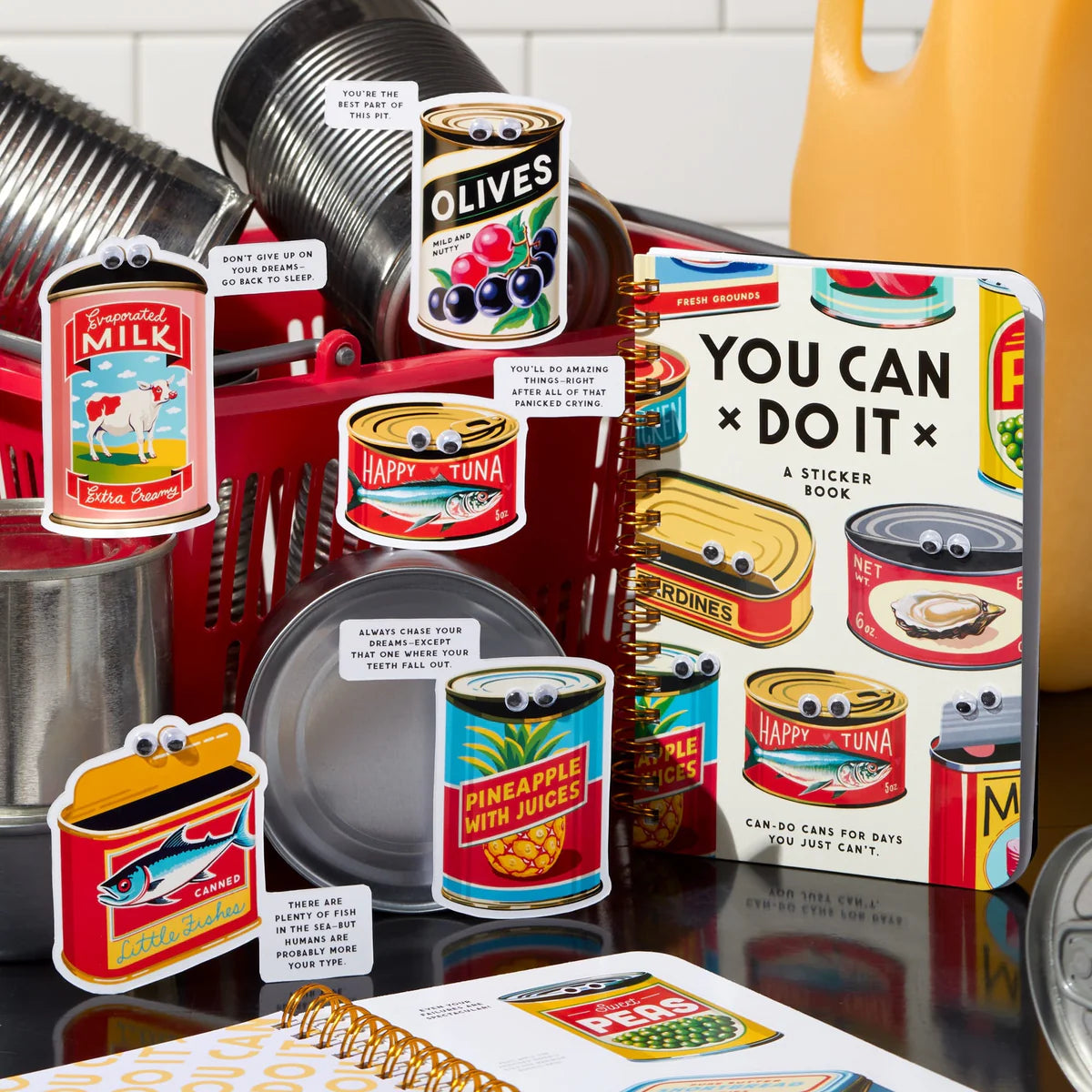 Collection of vintage-style food stickers and a 'You Can Do It' book on a reflective surface.
