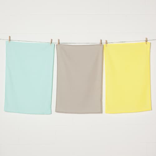 3 flour sack dishtowels hanging on line with clothespins: one each of jade, taupe, and yellow.