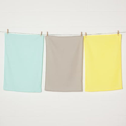 3 flour sack dishtowels hanging on line with clothespins: one each of jade, taupe, and yellow.