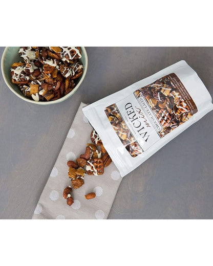 A bag of snack mix with chocolate laced with nuts and cereal pieces spilling out onto a cloth.