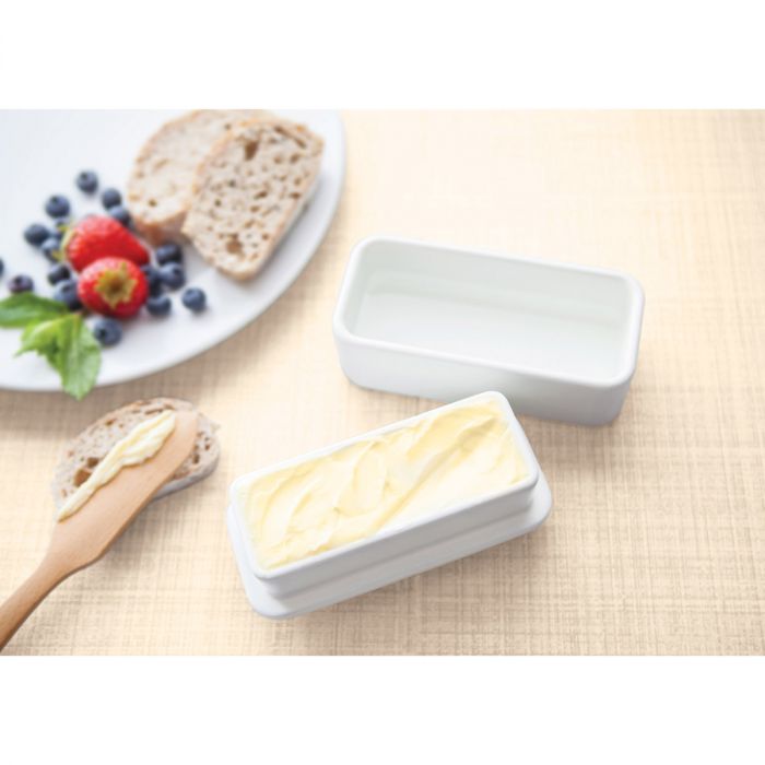 the full stick butter keeper filled with butter sitting on a light surface next to bread slices and a spreader