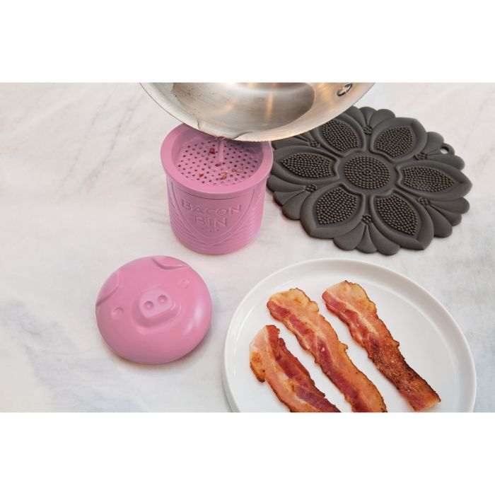 the grease holder displayed next to a plate of bacon with grease being poured from a skillet on a white background