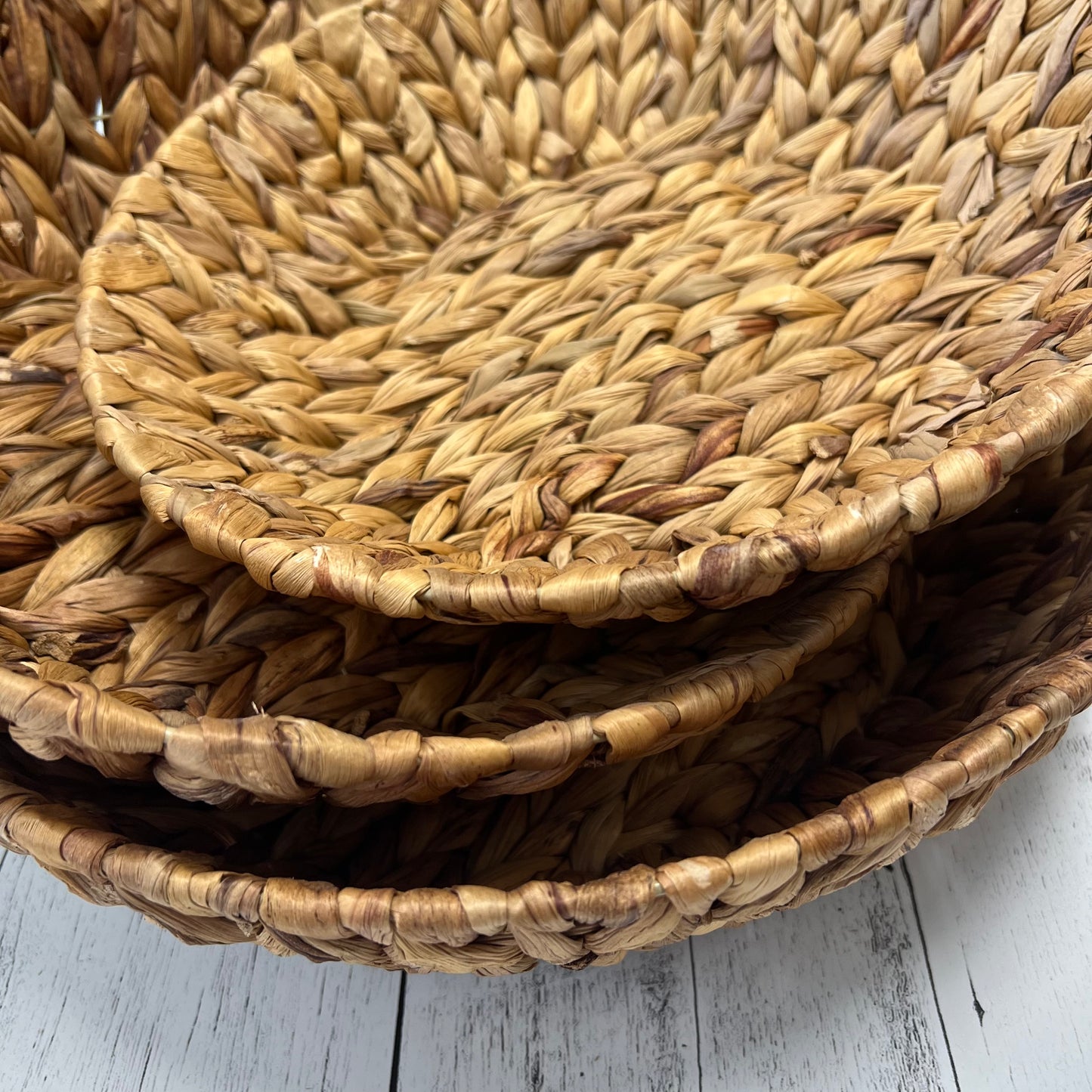 side view  of 3 sizes of hyacinth baskets on a white wooden background.