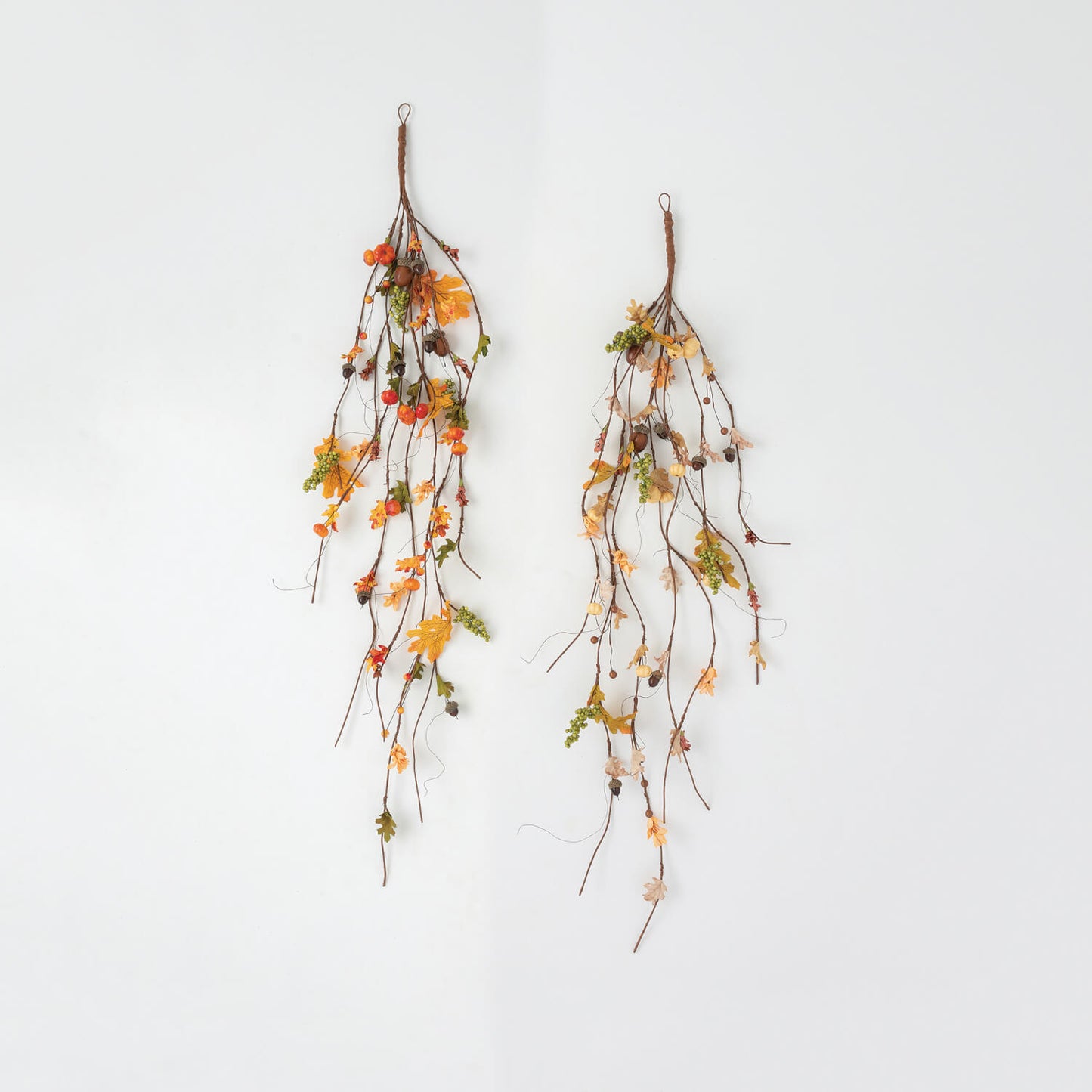 two hanging stems with artificial leaves and berries on white background.