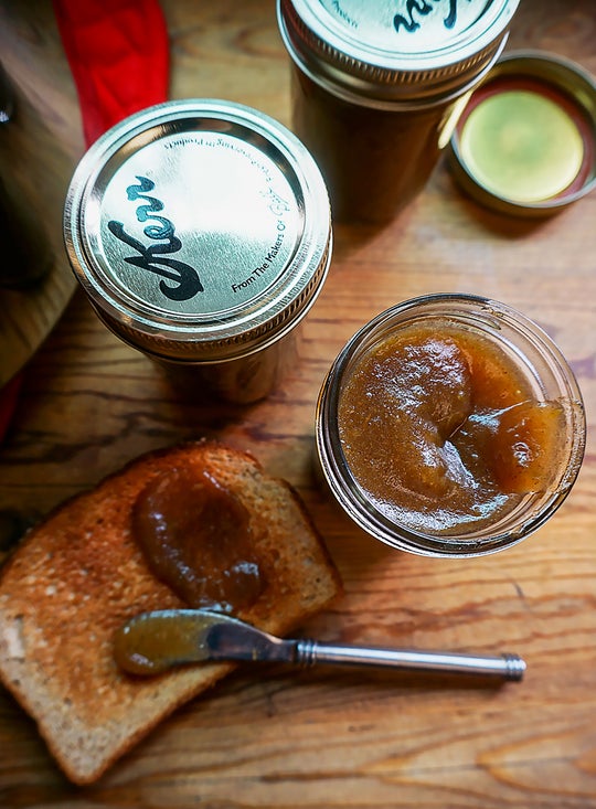 jars of jam, slice of toast, and stainless steel spreader on wood table.