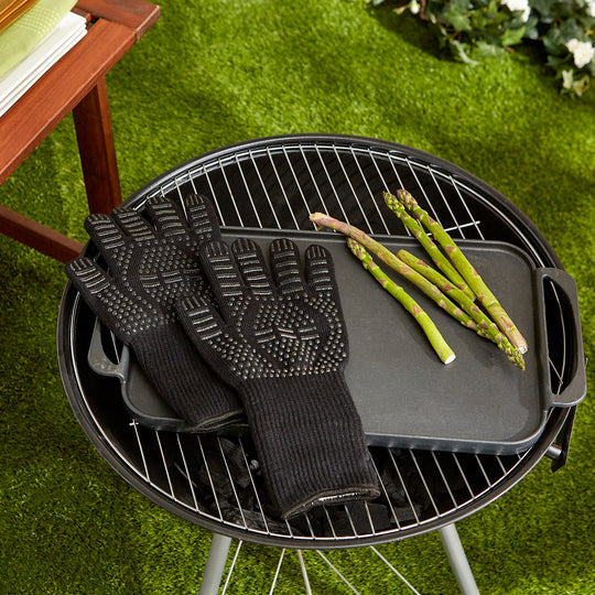 pair of grill gloves laying over the grates of a round grill sitting outside