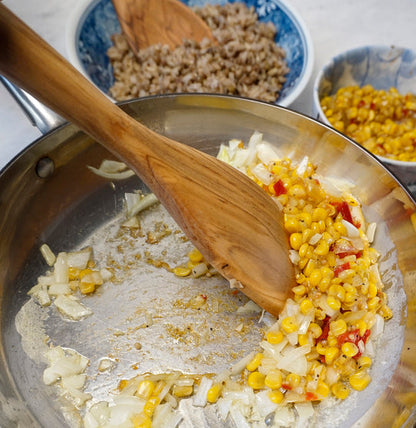 olive wood spatula being cooked with in a stainless steel skillet with corn and onions