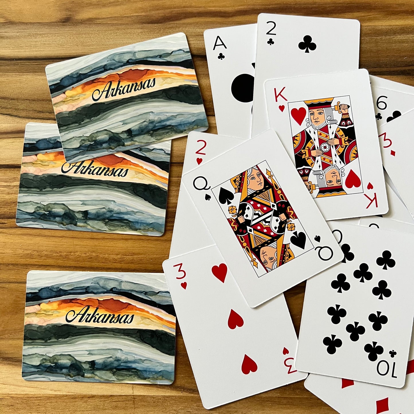 playing cards arranged on a wooden table, some are face up, others are face down showing sunrise image and "arkansas" printed on them.