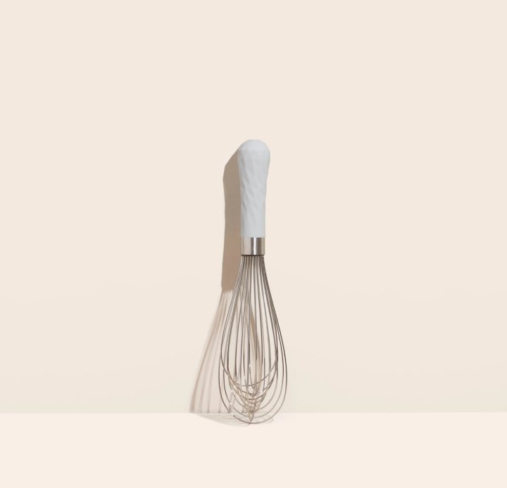 ultimate whisk leaning against a cream colored background.