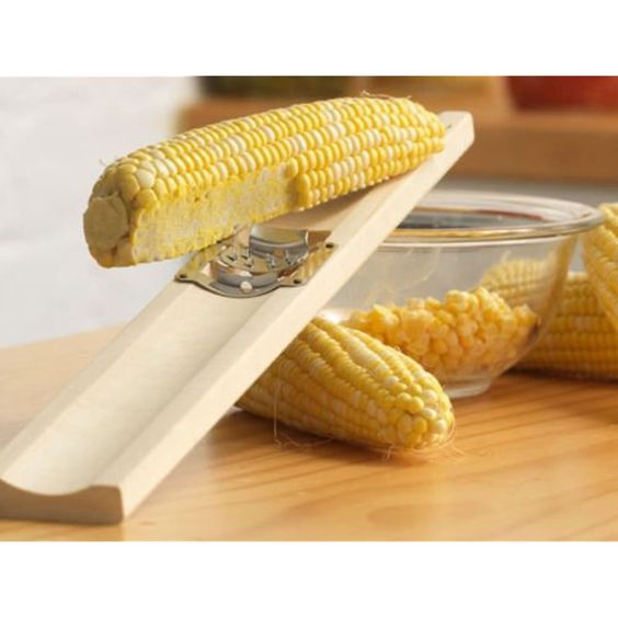 the corn cutter displayed with ears of corn and a bowl on a wooden surface