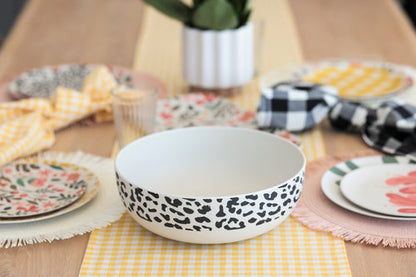 table setting with cheetah print serving bowl in center with plates and placemats on either side and greenery in the background.