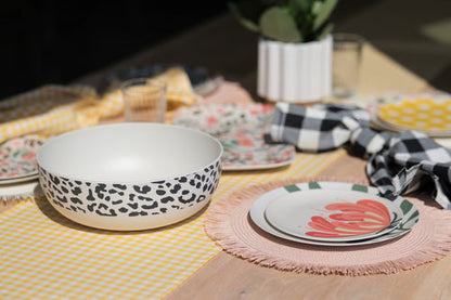 table setting with plates, placemats, napkins, and greenery in background with black cheetah print serving bowl in foreground.