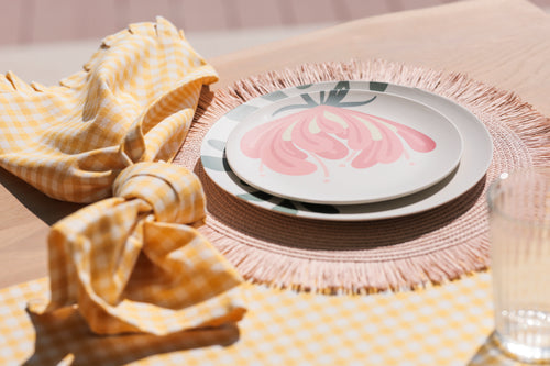 table setting with leafy dinner plate, flower salad plate, blush fringed placemat, and yellow checkered napkin.