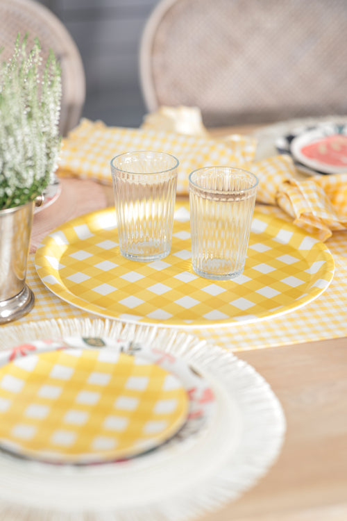 tabletop scene with plates and placemats, yellow check tray with glasses on it, and vase of flowers.