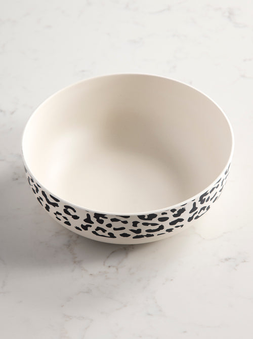 angled view of ivory bowl with black cheetah print rim on a marble background.