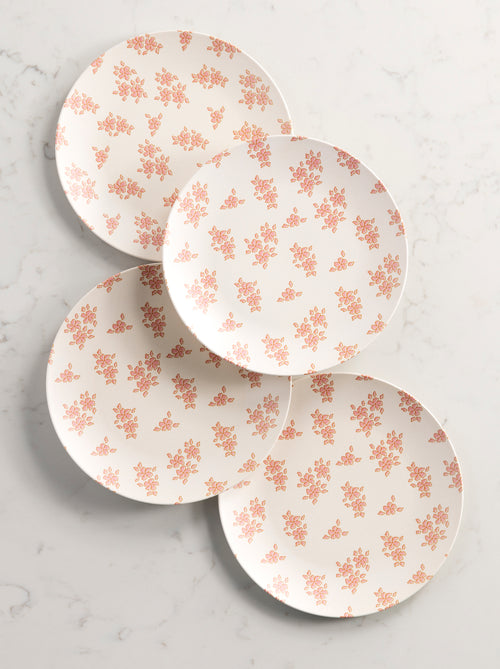 4 ivory dinner paltes with pink flowers arranged on a marble background.