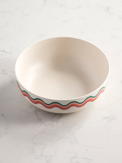 angled view of large serving bowl with wavy colorful pattern around outer rim on marble background.