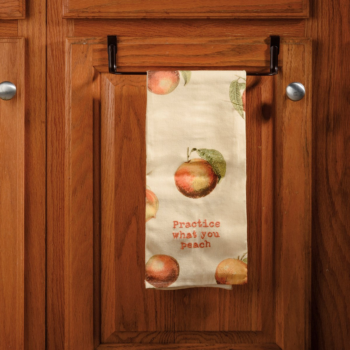 ivory towel with peach design hanging on a bar on kitchen cabinets.
