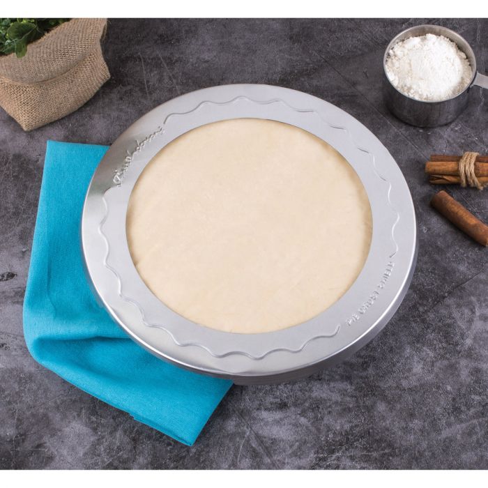 the 10 inch pie crust shield displayed on a pie next to apples cinnamon sticks and a gray surface