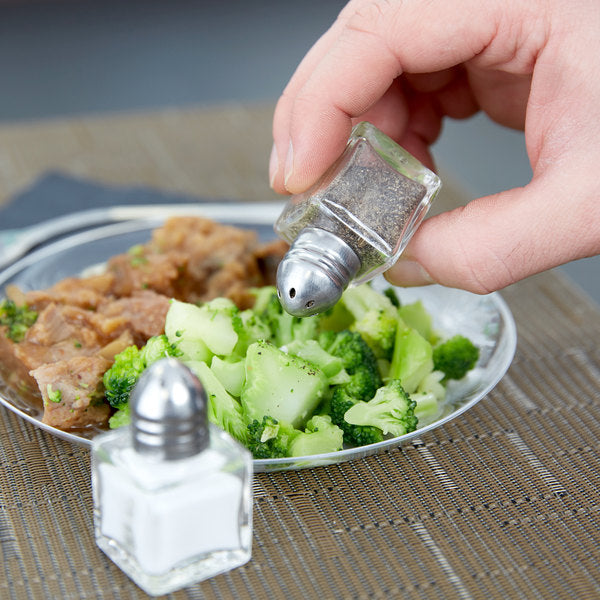 hand holding shaker filled with pepper shaking over plate of food.