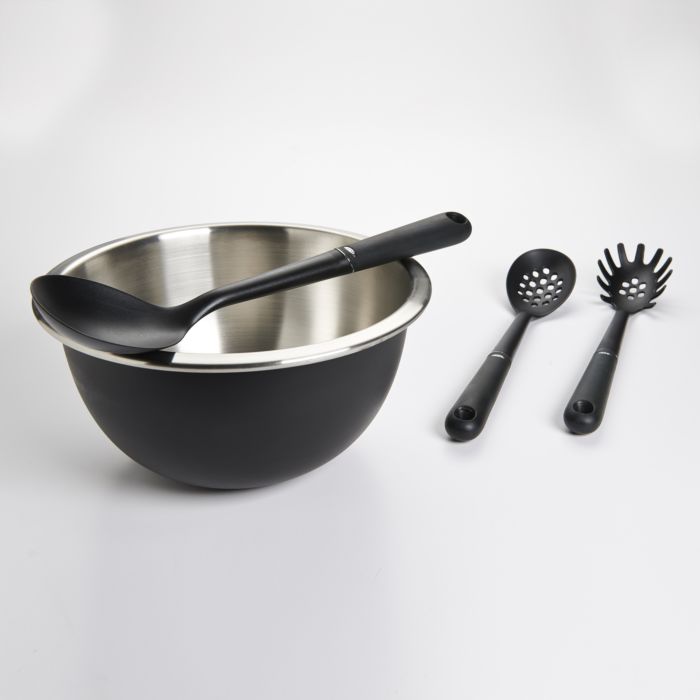 spoon set across mixing bowl with slotted spoon and pasta fork next to it.
