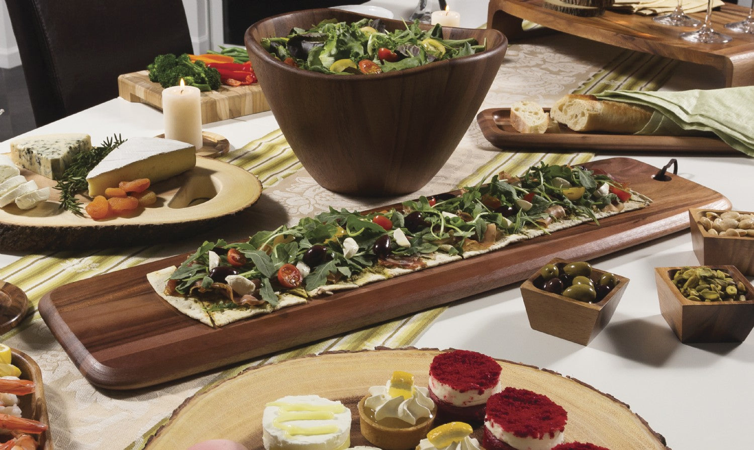 table setting with the acacia wood serving board next to a wood salad bowl round charcuterie boards filled with foods on a striped tablecloth