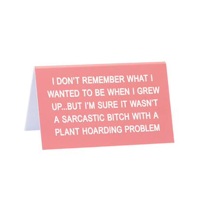 pink funny desk sign with text "I don't remember what I wanted to be when I grew up... but I'm sure it wasn't a sarcastic bitch with a plant hoarding problem" against a white background