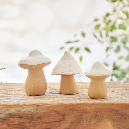 all three sizes of white top with tan stem cone mushrooms displayed on a rustic cut log with a shrub in the background