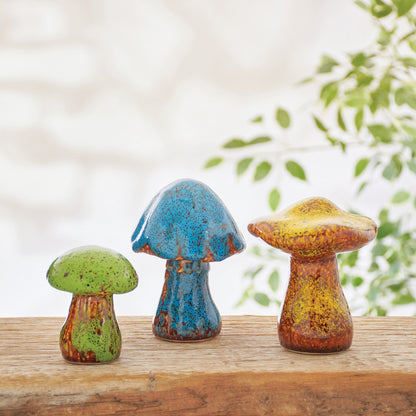 3 sizes of colorful mushrooms on a wooden ledge with greenery on the background.