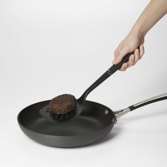 hand holding turner with burger on it over fry pan.
