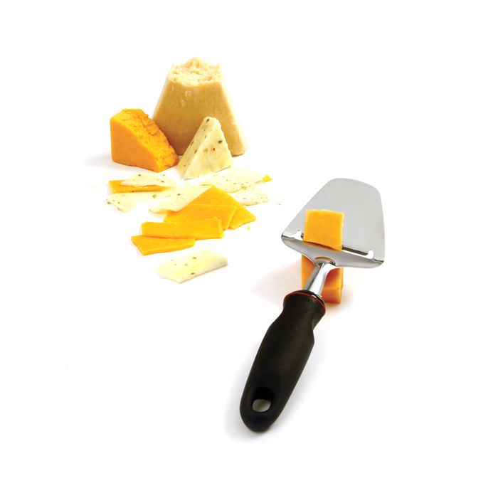 cheese slicer slicing cheese with blocks and slices of cheese in background.