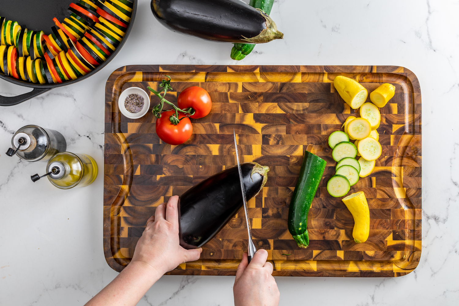 illustration of a person chopping vegetables on the acacia end grain board with juice groove next to salt and pepper grinders and pan filled with sliced veggies on a white countertop