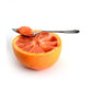 spoon with piece of grapefruit on it resting across half a grapefruit.